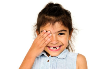 young girl covering one eye missing several baby teeth
