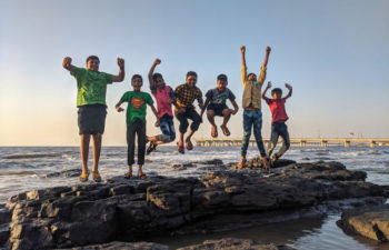 7 young boys frolicking on a rock in the surf