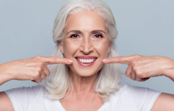 white haired woman pointing at her smile makeover with both forefingers