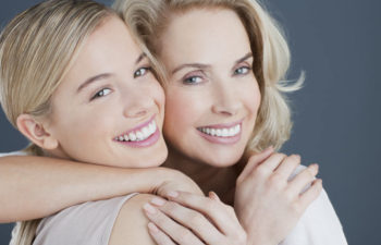 two blond women hugging and smiling after learning about cosmetic dentistry