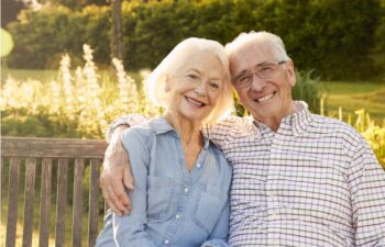 senior couple sitting on a bench hug and smile after learning about the benefits of dentures