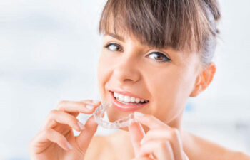 woman smiles as she inserts her Invisalign clean aligner