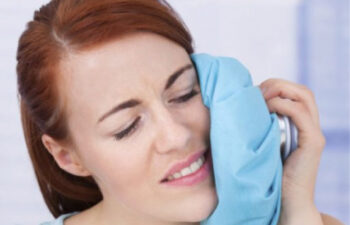 woman holds an icepack to her jaw recovering from a tooth extraction