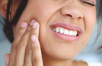 woman holds her cheek in pain from a tooth infection needing a root canal