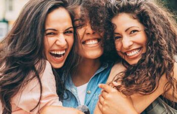 three young women hug and smile showing off their great smiles