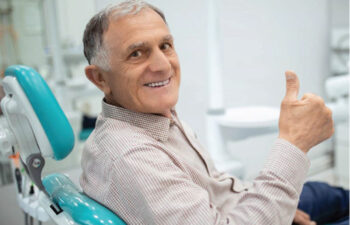 senior man gives a thumbs up in the dentist chair after learning about tooth replacement options