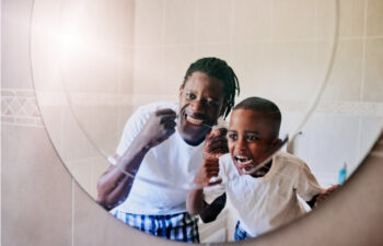 man and his young son floss their teeth together