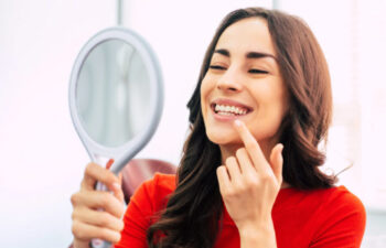 woman holds a hand mirror and looks at her teeth whitening results