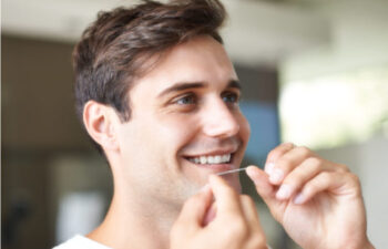 young man smiles while flossing his teeth
