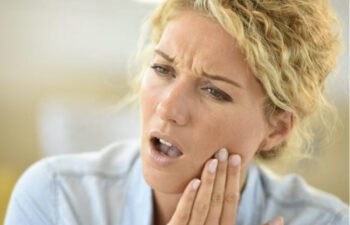 blonde woman holds her jaw in pain from TMJ disorder