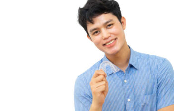 young man smiles and holds up his clear aligner