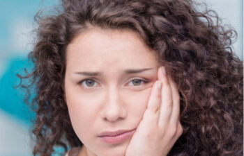 young girl holds her cheek in pain with a toothache