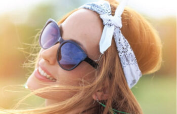young woman wearing sunglasses and a head scarf smiles showing off teeth whitening results