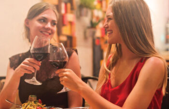 two young women toast with glasses of red wine